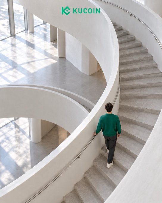 A man in a green sweater climbs a sweeping spiral staircase in a bright, modern interior, visually embodying the post's message of steady, deliberate upward progress. The KuCoin logo appears at the top, reinforcing the brand's association with consistent, incremental growth rather than rapid leaps.