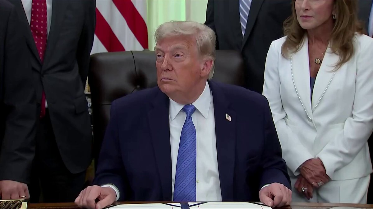 The image shows a man sitting at a desk, wearing a suit and tie, with his hands resting on the table. The scene takes place during a meeting or conference where several people are present, including a woman standing behind him. The background features an American flag, suggesting that this gathering might be taking place in the United States.

The image also includes text that reads "Better not see anyone saying stablecoins protect you from inflation ever again. Simply tragic they've been ramrodded into Bitcoin wallet apps." This statement seems to be related to the ongoing discussion or event happening in the scene, possibly discussing the impact of Bitcoin and other cryptocurrencies on traditional financial systems.

The image captures a moment where people are engaged in conversation or decision-making, with the man at the desk as the central figure.