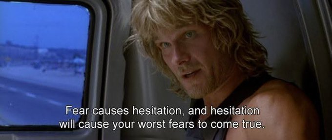 A blonde man with a rugged appearance sits inside what appears to be a vehicle, with a caption reading "Fear causes hesitation, and hesitation will cause your worst fears to come true." The image relates to the post's theme of overcoming fear in investing—pushing past hesitation to buy during market recoveries instead of letting fear paralyze decision-making.