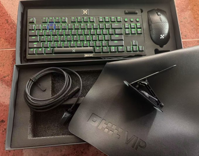 A Razer BlackWidow V4 mechanical keyboard with green backlighting and a Razer DeathAdder V3 mouse are displayed in their packaging alongside an aluminum phone stand, a coiled cable, and a custom OKX VIP desk mat. The image showcases the premium gaming bundle gifted for achieving OKX VIP status, featuring the OKX VIP logo on the desk mat and matching the post's description of the exclusive Razer esports set.