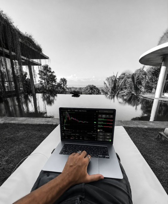 A person uses a laptop showing cryptocurrency trading charts while relaxing by an infinity pool, with "$sato" ticker suggesting Satoshi/Bitcoin-related trading activity.