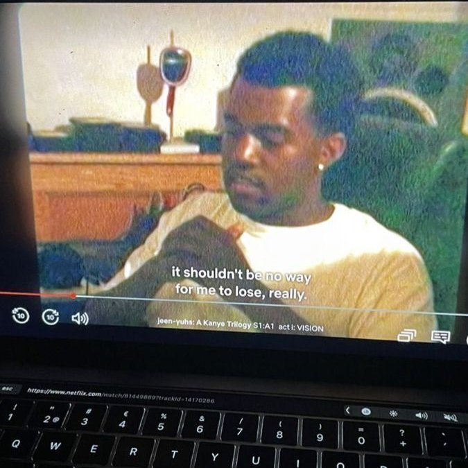 Photo of a laptop screen playing a Netflix video titled 'Jeen-yuhs: A Kanye Trilogy S1:A1 act I: VISION', showing a young Kanye West with the subtitle 'it shouldn't be no way for me to lose, really.'