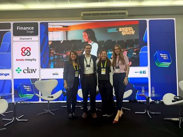 Four women wearing lanyards posing together at a corporate event booth, with screens displaying 'Finance Vertical Channel & Awards Integrity' and logos including 'clav' and 'Getac'.