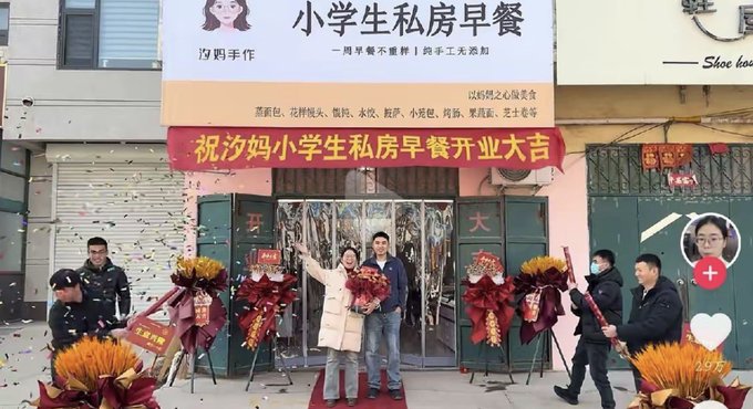 A storefront opening ceremony for '小学生私房早餐' (Xiaomom's Private Breakfast) with a red banner congratulating the grand opening and floral arrangements.