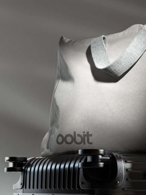 A minimalist product photo of a light gray "oodbit" canvas tote bag resting on top of a black hard-shell suitcase against a gray background.