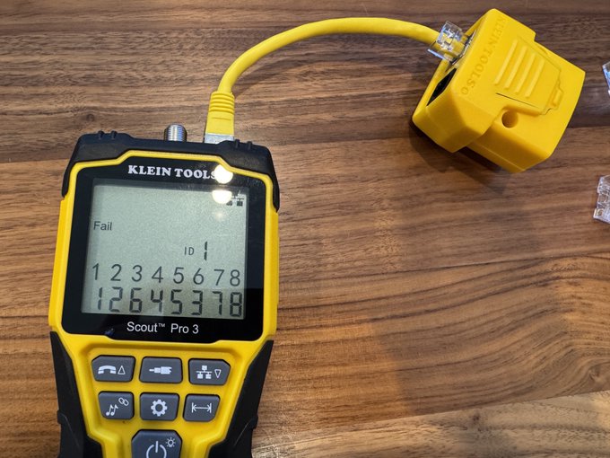 A Klein Tools Scout Pro 3 cable tester displays 'Fail' on its screen with the numbers 12345678 and 12645378, connected via a yellow cable.