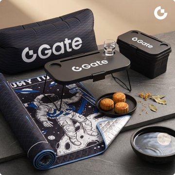 A product display featuring a GGate picnic blanket set with a black carrying case, matching pillow, and a folding table branded with the GGate logo, alongside mooncakes and a glass.