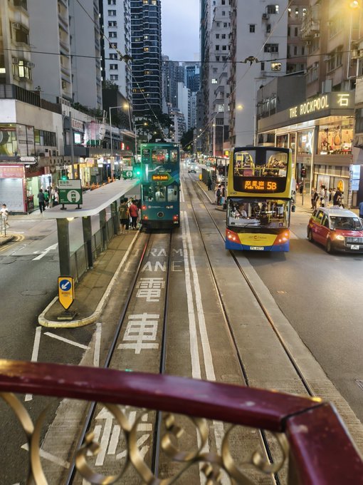A street view in Hong Kong featuring two double-decker trams on tracks, with 'RAM CAR LANE 電車' painted on the road and 'THE ROCKPOOL' storefront visible on the right.