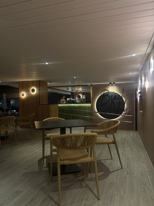 A dimly lit restaurant interior featuring wooden slat ceilings, woven rattan chairs around dark tables, and a backlit circular sign reading "Bushi" — a moody, stylish setting perfect for a late-night "GN" (good night).