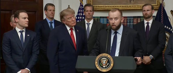 A press conference at the White House featuring President Donald Trump and other officials, with a man speaking at a podium bearing the Presidential seal.