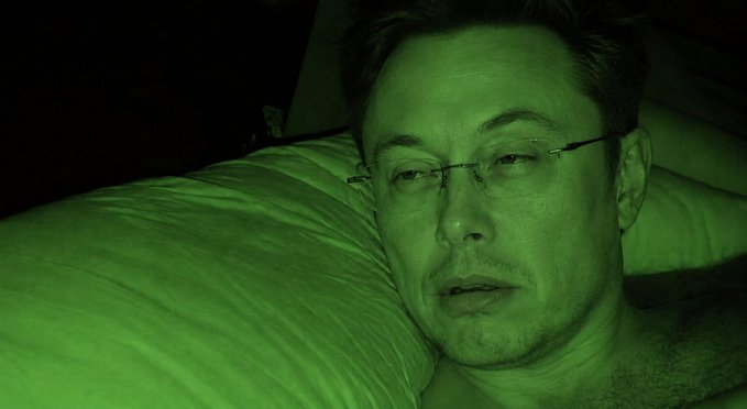A close-up selfie of a man lying on a white pillow, viewed through green night-vision style filter.