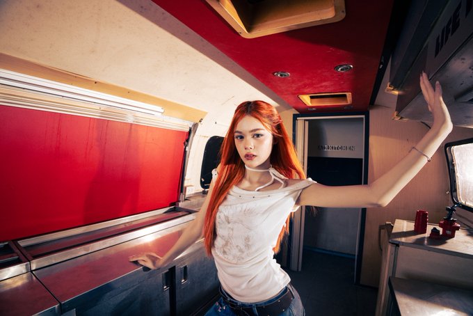 A red-haired woman posing inside a food truck or similar vehicle, leaning against the counter.