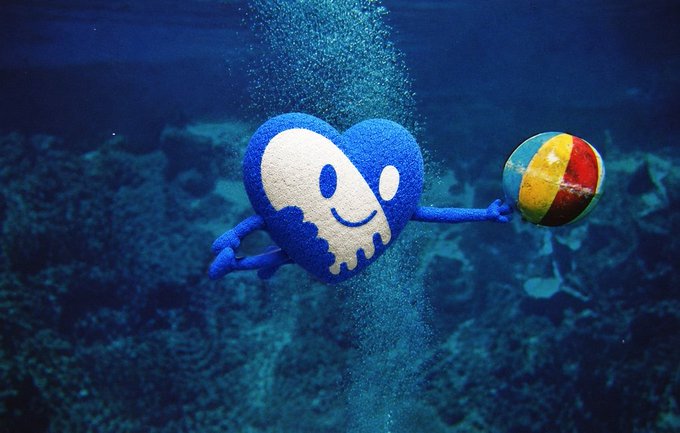 A blue plush heart-shaped toy with a smiling face holds a colorful striped beachball underwater, surrounded by rising bubbles. The image playfully illustrates the post's message about taking chances, with the cheerful character and beachball symbolizing fun, optimism, and a willingness to embrace the unknown.