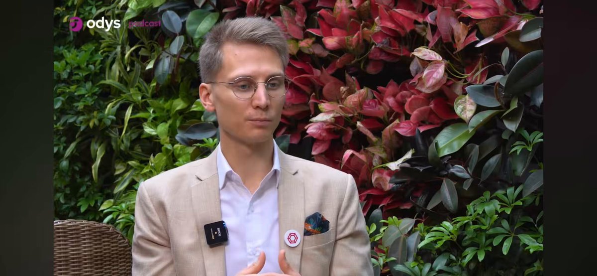 The image features a man wearing glasses, standing against a backdrop of red flowers and greenery. The man appears to be dressed in a suit or a white jacket, with his hands placed on his hips as he looks directly at the camera. The background is filled with various plants and flowers, creating an impression of a garden setting.

The image also contains text that reads "Marcin Kaźmierczak co-founder @redstone_defi We are at an inflection point". This phrase suggests that there might be a significant change or transition happening in the man's life or career, and he is contemplating this change while standing amidst nature.