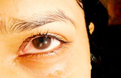 Close-up of a person's brown eye with visible eyelashes and eyebrow against dark hair.