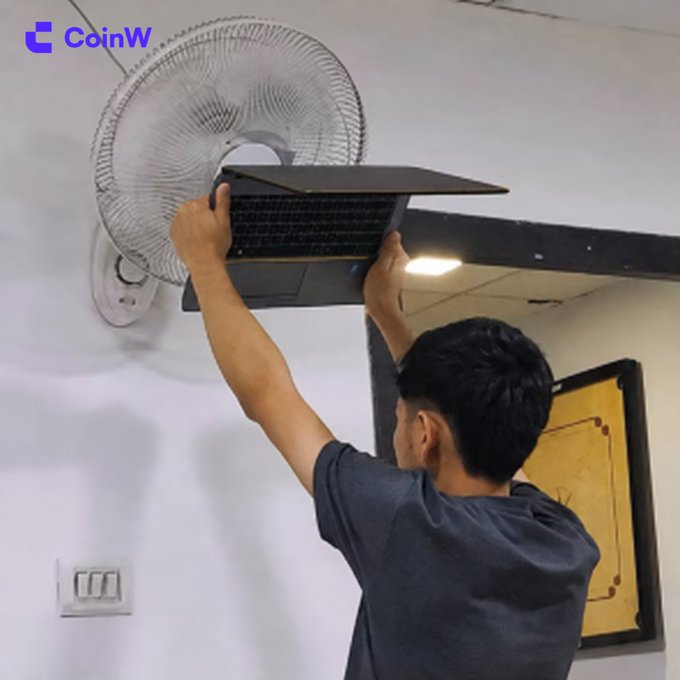 A man holds a laptop directly in front of an oscillating wall fan, appearing to use the air to cool his overheating device. The "CoinW" logo is visible in the top left corner.

The image humorously illustrates the post's theme of a trader's panicked, last-ditch effort to cool down an overworked computer after a sudden portfolio dip—jokingly acting as if blowing on the laptop will somehow fix the losses.