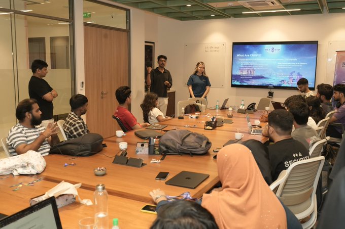 A group of people gathered around a long conference table in a meeting room, with two individuals standing and presenting in front of a screen displaying "What are CASSFs?"