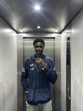 A man in a denim jacket taking a mirror selfie with his phone inside an elevator.