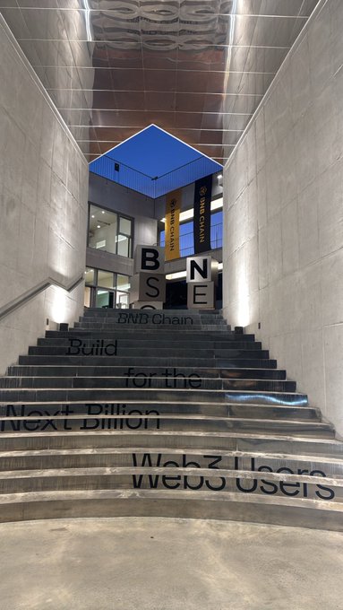 A modern staircase features text reading 'BNB Chain Build for the Next Billion Web3 Users' with BNB Chain banners visible at the top of the stairs.