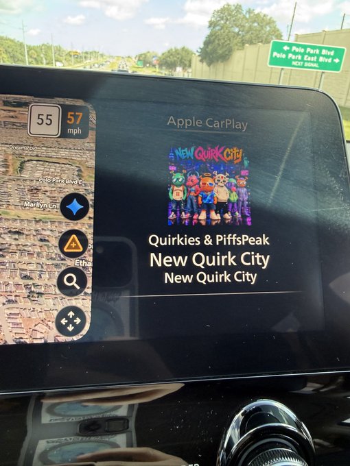 A car's dashboard screen displays Apple CarPlay playing "New Quirk City" by Quirkies & PiffsPeak, with a speed indicator showing 55-57 mph and a road sign for "Polo Park Blvd." visible through the windshield.