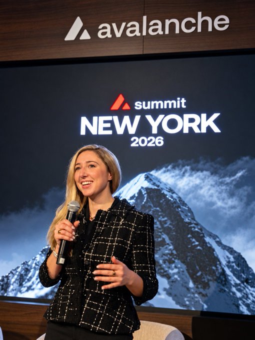 A blonde woman in a black tweed jacket speaks into a microphone on the Hudson stage at the Avalanche Summit New York 2026, as she introduces the day's tokenization talks.
