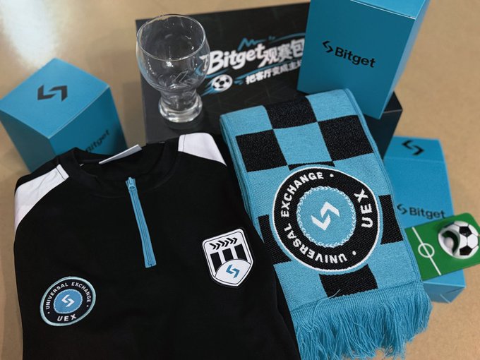 A black "Universal Exchange (UEX)" jersey and a black-and-blue checkered scarf featuring the "EXCHANGE • UNIVERSAL EX•" logo are displayed alongside a clear glass goblet, a soccer ball pin, and "Bitget" branded boxes, matching the World Cup viewing package sent by @Bitgetyaya and @Bitget_zh for watching the games.