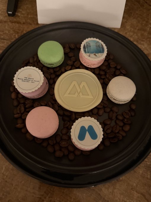 A black plate displays colorful macarons (green, pink, purple) with Metroboomin branded wrappers, a chocolate disc with the Metroboomin logo, and coffee beans.