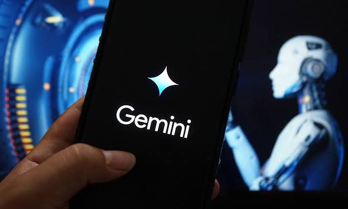 A hand holding a smartphone displaying the Gemini AI logo, with a blurred humanoid robot in the background.