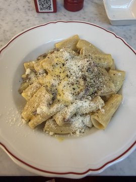 A plate of rigatoni pasta topped with a raw egg yolk, butter, and grated cheese—classic carbonara—is shown alongside a QR code menu on a marble counter, apparently enjoyed during a meal break at the "Monk Monk War Room for Launch" event in Milan.