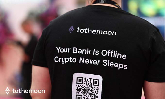 The back of a person wearing a black 'tothemoon' branded t-shirt with text 'Your Bank Is Offline / Crypto Never Sleeps' and a QR code.