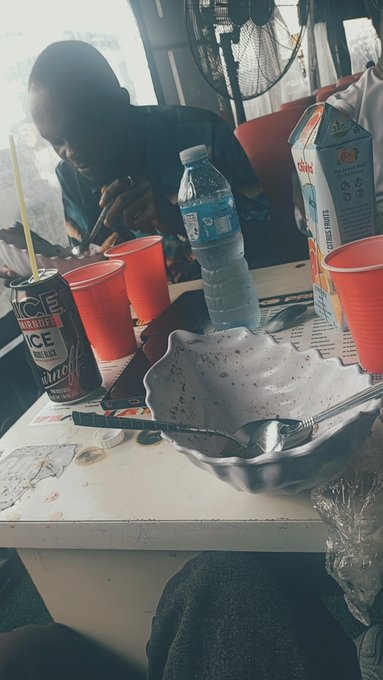 A casual scene at a table with red Solo cups, a water bottle, an ICE beer can, and a candy box, while a person looks down at their phone.