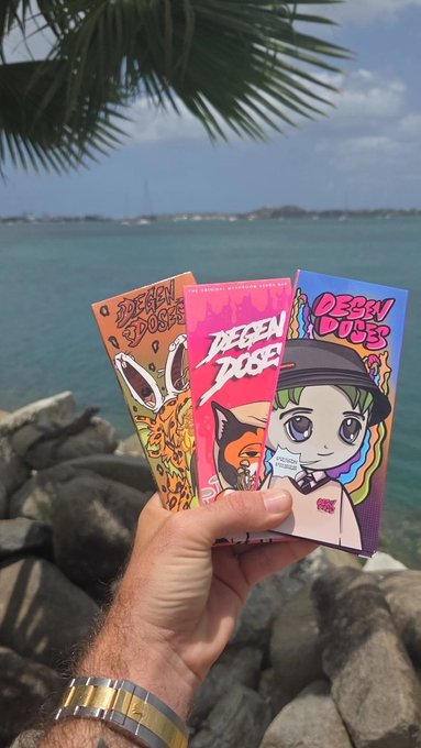 A hand holds three colorful commemorative tickets or cards featuring the text 'DEGEN DOSE' against a tropical ocean backdrop.