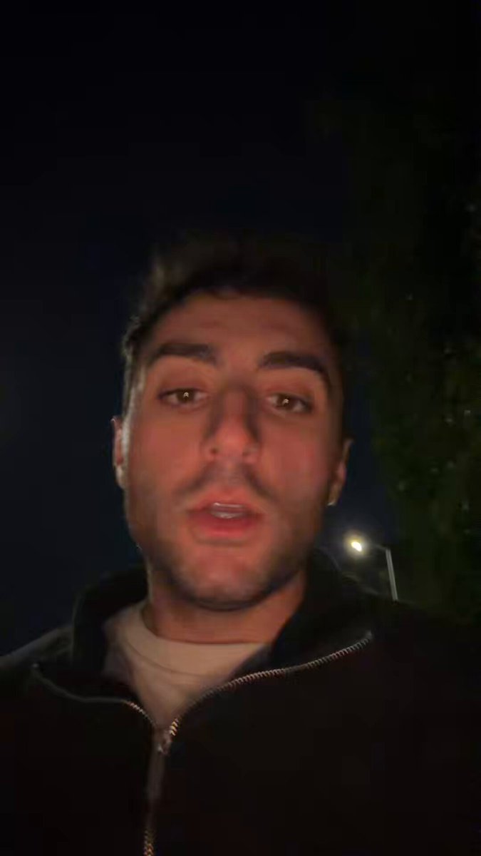 The image features a man wearing a black jacket with his face turned towards the camera. The background of the photo shows a dark sky, which contrasts with the man's attire. There are no texts or other objects present in the image, making the focus solely on the man and his expression as he looks directly at the camera.