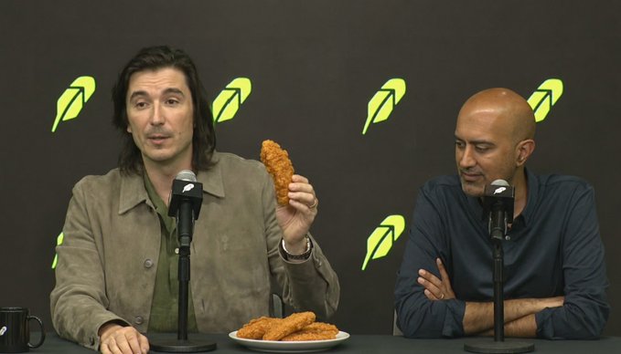 Two men seated at a podcast table with microphones and a plate of fried chicken, with green leaf logos in the background.