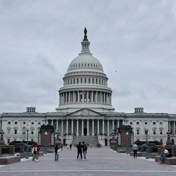 The United States Capitol building in Washington D.C. with its iconic white dome and columns, viewed from the front plaza with visitors walking around.