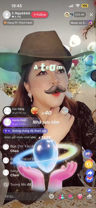 A TikTok livestream by user "C.Ngy6666" features a woman wearing a cowboy hat, a drawn-on mustache, and a veil, with "A team" displayed on her forehead. The screen shows 353.4K viewers and comments like "menly thoit" and "Cục Đắng," aligning with the post about waiting with 500K viewers for the livestream.