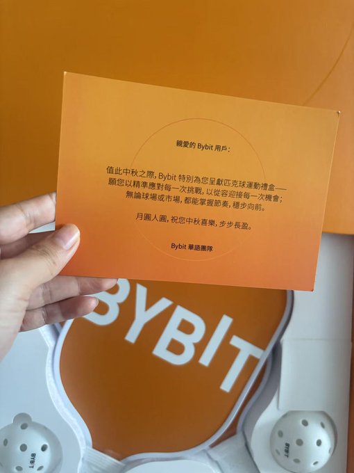 A hand holds an orange card with Chinese text from Bybit wishing the user a Happy Mid-Autumn Festival, above what appears to be a Bybit-branded VR headset.