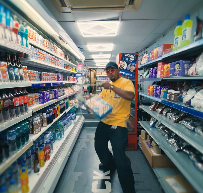 A man in a yellow shirt dances down a convenience store aisle holding a bag of chips, with a MoonPay x rekt drinks promotional sign visible in the background featuring the text "THE CALL UP" and "LIVE ON X," matching the post's mention of the MoonPay x @rektdrinks collaboration.