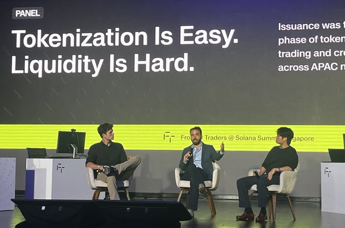 Three men seated on stage during a panel discussion at a Solana Summit in Singapore, with a large screen behind them displaying the text 'Tokenization Is Easy. Liquidity Is Hard.'