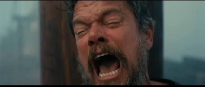 A close-up cinematic shot of a bearded man with his eyes closed, mouth wide open in an intense scream or shout.