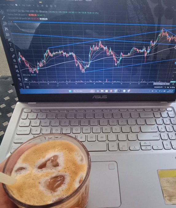 An ASUS laptop displaying a BTC/USDT candlestick chart on TradingView with a rising wedge pattern, accompanied by a Vietnamese coffee with condensed milk in the foreground.