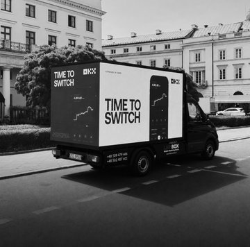 A black and white photo of a delivery truck branded with "TIME TO SWITCH" and the OKX logo, with "EILANDMARK" and phone number "+45 21 54 84" visible on the side, parked in an urban European street setting. The truck's branding aligns with the post's announcement of OKX launching an in-person activation tour across major European cities to mark July 1st, promoting regulatory clarity for digital assets.