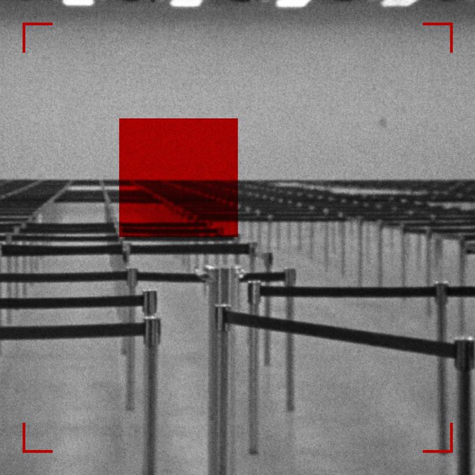 Black and white surveillance-style image with a red square in the center and red corner brackets, showing what appears to be a parking lot barrier or gate structure.
