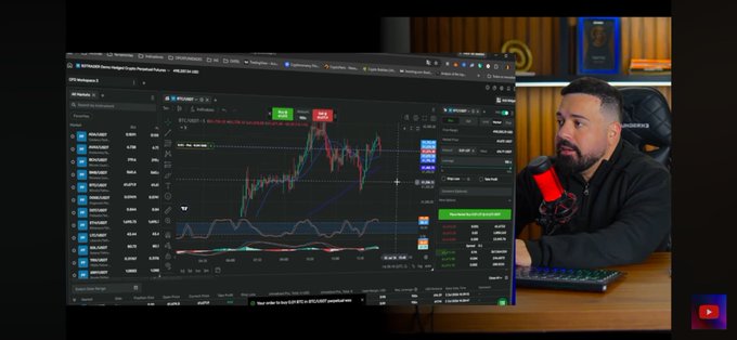 A man sits at a desk in front of a microphone with a computer screen displaying a BTC/USDT trading chart on Binance, showing various candlestick patterns and technical indicators.