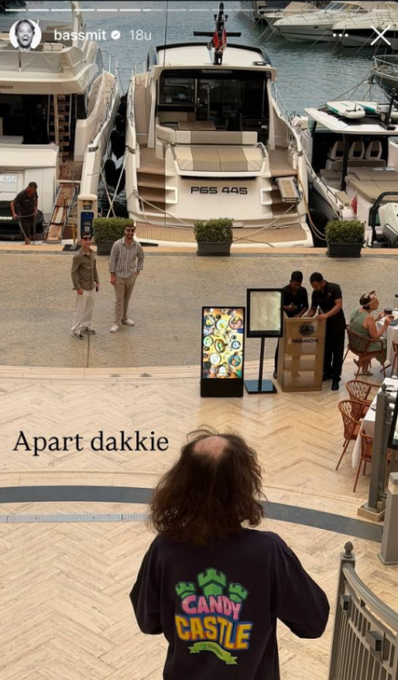 A view from above showing a person in a 'CANDY CASTLE' shirt looking out at a marina with yachts, with a Snapchat story overlay from 'bassmit' and text reading 'Apart dakkie'.