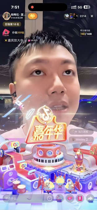 Mobile livestream screenshot showing an East Asian man with overlaid graphics including '喜人DO', a small stadium scene, viewer counts like '2214', and a heart icon '62'.