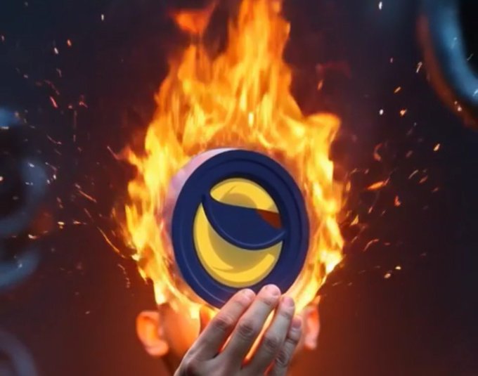A hand holds up a circular blue and yellow logo engulfed in flames and surrounded by sparks against a dark background.