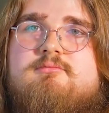 A close-up of a bearded man with round glasses looking slightly off-camera.