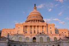 A wide-angle view of the U.S. Capitol building bathed in warm sunset or sunrise light, showing its grand white dome and columned facade.