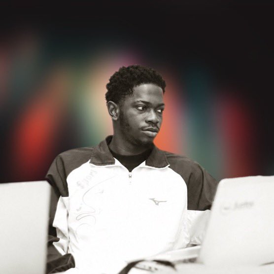 A black and white photograph of a young man in a white and dark jacket sitting at a computer, with his image and the background artistically colorized.